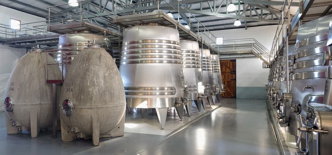Perspectiva del pasillo de la bodega con huevos de hormigón en primer plano y tanques de acero inoxidable al fondo