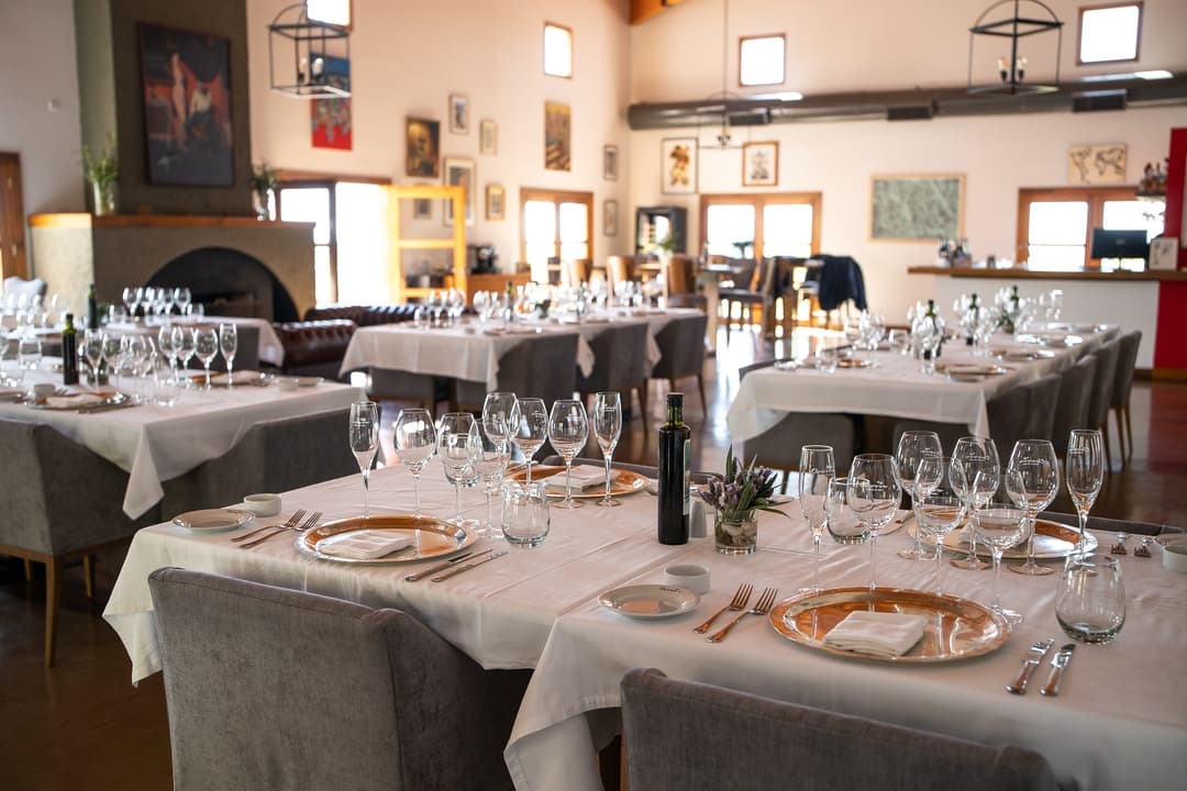 Salon preparado para evento con mesas vestidas, cristaleria y chimenea encendida